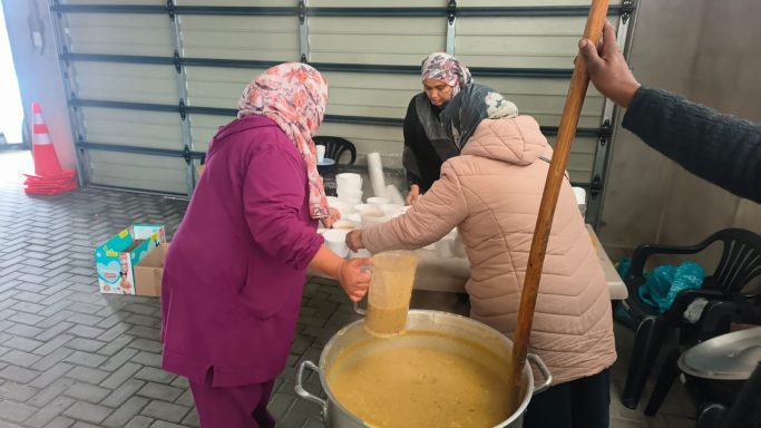 Women preparing food in a large pot in a community kitchen.