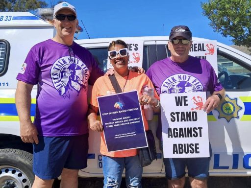 Three people holding signs for a protest against abuse, with police vehicle in the background.