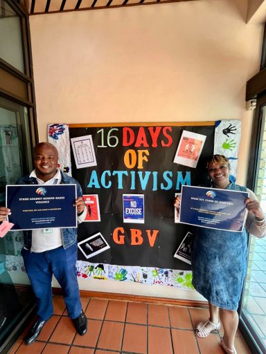 Two individuals holding certificates stand in front of a display for "16 Days of Activism GBV."