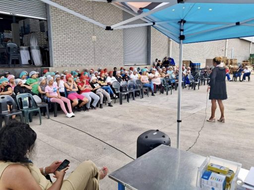 A speaker addresses a seated audience under a blue tent.