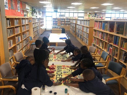 Children gathered around a table in a library, engaged in a creative activity.