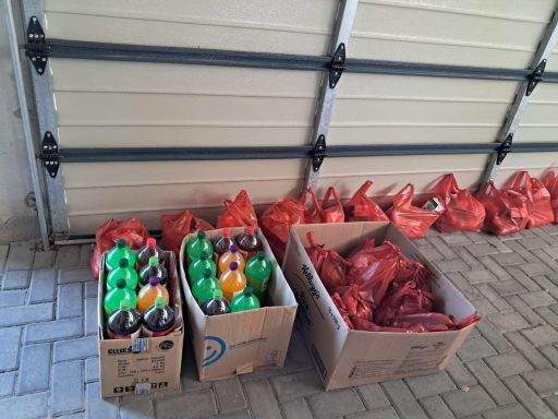 Boxes of colourful balls in green, orange, and red arranged on a paved floor.