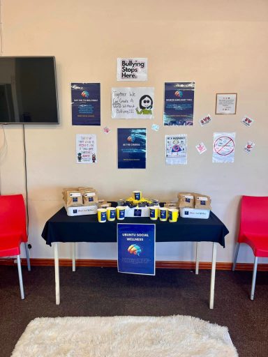 A table with yellow and blue items, surrounded by posters and red chairs.