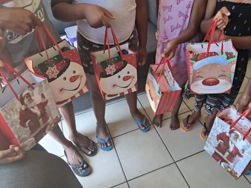 Children holding festive gift bags with snowman and Christmas designs.